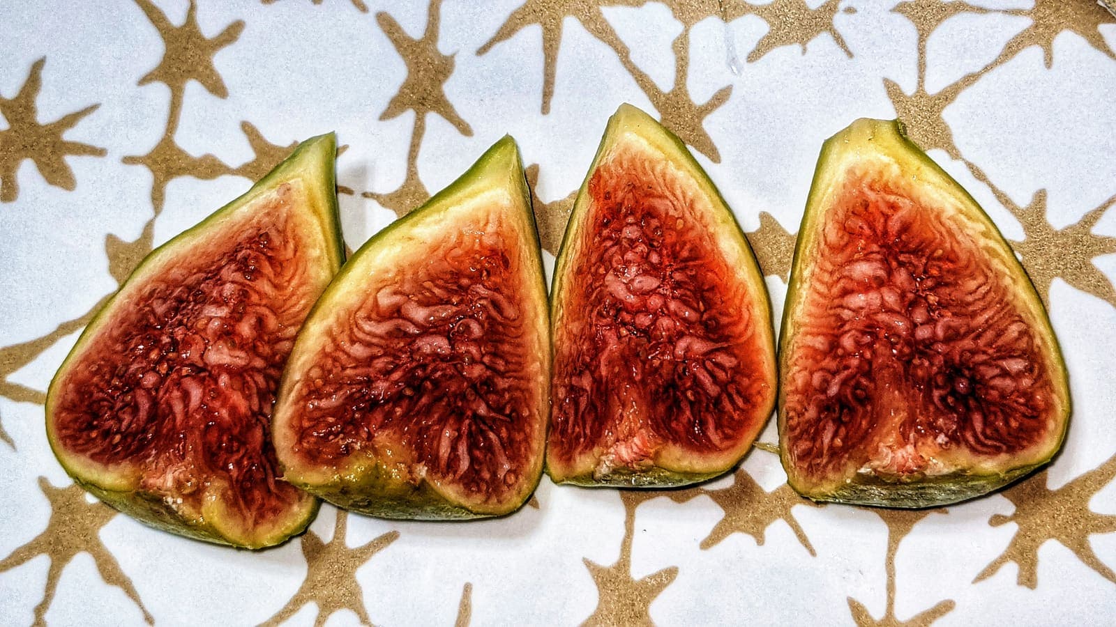 Four ripe fig quarters in a row, showing their jammy red interiors.
